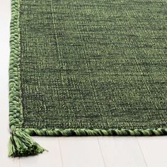 a green rug with tassels on the bottom and sides, laying on a white floor