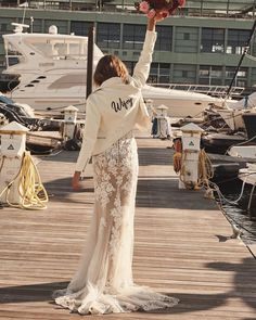 a woman in a white jacket and dress standing on a dock next to some boats