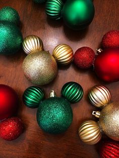 many different colored christmas ornaments on a wooden table with red, green and gold balls