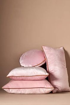 pink pillows stacked on top of each other in front of a beige wall and tan background