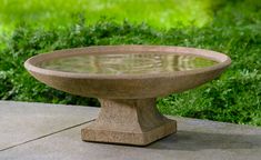 a stone bowl sitting on top of a cement table in front of green grass and bushes