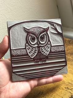 a hand holding an owl carved onto a piece of wood on top of a wooden table