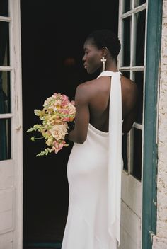 a woman in a white dress holding a bouquet of flowers and looking out the window