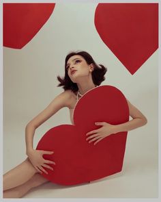 a woman sitting on the ground holding a red heart shaped object in front of her