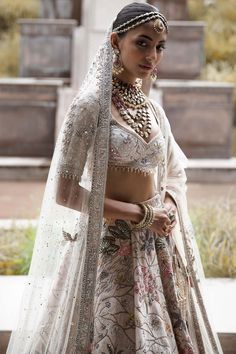 The vintage udaibagh lehenga showcases nature-inspired motifs on an off-white raw silk base, stealing the spotlight with multi-coloured resham aari, tarnished dori work, and intricate hand embroidery using nakshi, dabka, sequins, mirrors, and zardozi. This modern masterpiece is elegantly paired with a net dupatta and veil, adding a touch of timeless grace to your ensemble. Off White Lehenga, Cut Work Blouse, Lehenga And Blouse, White Lehenga, Raw Silk Lehenga, Indian Bridal Photos, Royalty Aesthetic, Designer Jumpsuits, Designer Dresses Indian