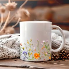 a white coffee mug with colorful flowers painted on the side sitting on a wooden table