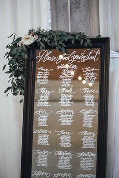 a wedding seating chart is displayed in front of a large mirror with greenery on it