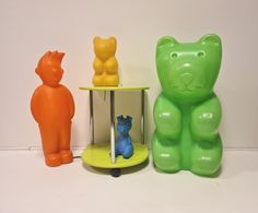 there are three plastic bears on the shelf next to each other, one is orange and one is green