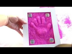 a person is holding up a pink handprint in a white frame with two small holes