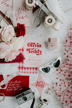 the contents of a wedding suite laid out on top of a white table with red and pink flowers