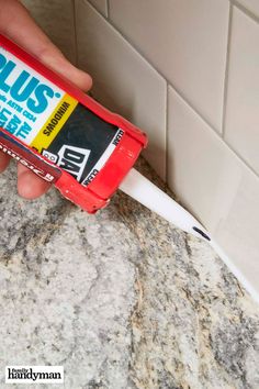 a hand holding a tube of glue on top of a marble counter next to a tile wall