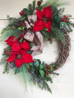 a christmas wreath with poinsettis and pine cones on a white wooden background