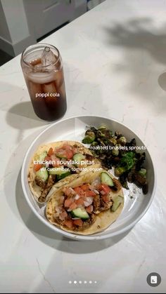 two tacos on a plate next to a drink