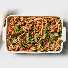 a casserole dish filled with pasta, spinach and sauce on a marble surface