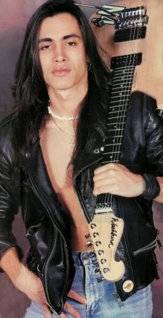 a man with long hair holding an electric guitar in his right hand and posing for the camera