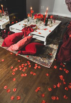 the table is set with red petals on the floor and candles are scattered around it