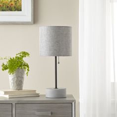 a table with a lamp and some books on it next to a plant in a vase