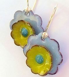 two blue and yellow flower shaped earrings with silver hooks on a white surface, set against a plain background