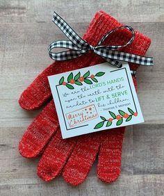 red gloves with a card attached to it on top of a wooden table next to a ribbon