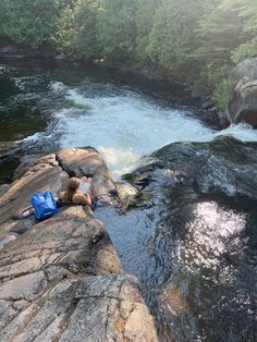 a person laying on top of a rock next to a river