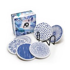 four blue and white plates sitting on top of a table next to a box of coasters