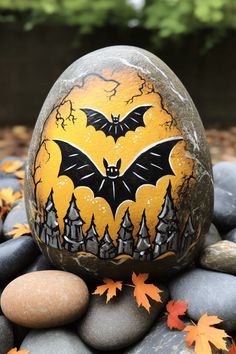 a painted rock sitting on top of some rocks with leaves around it and a bat