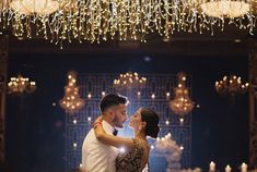 a man and woman are standing in front of a chandelier with lights on it