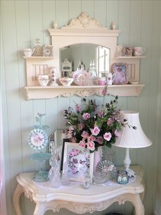 a white table topped with lots of vases and flowers next to a wall mounted mirror