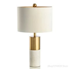 a table lamp with a white shade and gold trimmings on the base, against a white background