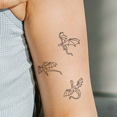 a woman's arm with three small tattoos on the back of her arm and one has a dragon tattoo on it