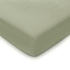 the side of a bed with a light green sheet on it and a white background