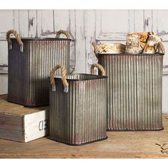 three metal canisters with rope handles on top of a wooden table next to each other