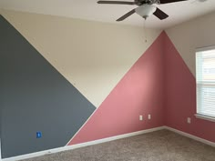 an empty room with a ceiling fan and pink, grey, and blue wallpaper