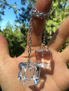 a hand is holding two clear cube pendants