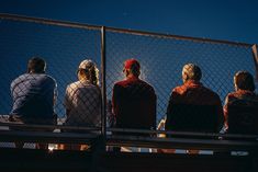 four people sitting on a bench looking out at the sky from behind a chain link fence