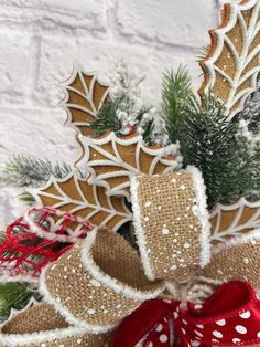 a christmas wreath with holly, pine cones and red ribbon hanging on a white brick wall