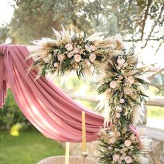 a wreath with flowers and feathers on it next to a candle in a wicker basket