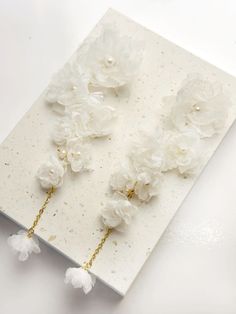 three white flowers are hanging from the side of a piece of paper with gold chains