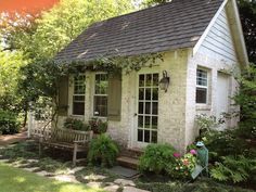 a small white brick house with green shutters and flowers on the front porch area