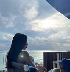 a woman sitting on top of a chair next to the ocean under a cloudy sky