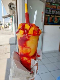 a person holding up a large cup filled with ice cream, fruit and sauces