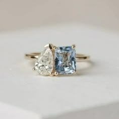 an engagement ring with two pear shaped blue and white diamonds on it, sitting on top of