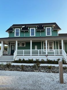 a large green house with white trim and porches on the front, covered in gravel