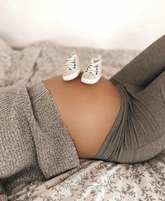 a pregnant woman laying on top of a bed wearing white tennis shoes and gray leggings