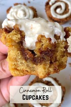 a person holding up a cupcake with white frosting on it and cinnamon rolls in the background