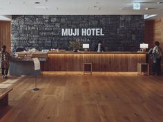 a hotel lobby with wood floors and stone wall behind the reception desk, there is a sign that says muji hotel