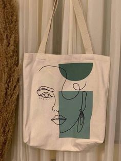 a white bag with a drawing of a woman's face on it hanging from a curtain