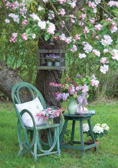 a chair and table in the grass under a tree with flowers on it, next to a potted plant