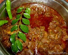 a metal bowl filled with meat and green leaves on top of a wooden table next to a pepper shaker