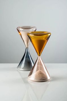 two glass vases sitting side by side on a white counter top, one has an orange and the other is silver